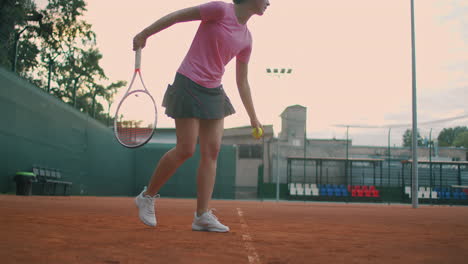 Low-angle-view-in-slow-motion-of-a-young-female-tennis-player-preparing-to-serve-a-tennis-match.-A-woman-athlete-is-powerfully-hitting-a-ball-during-sports-practice.-Commercial-use-footage